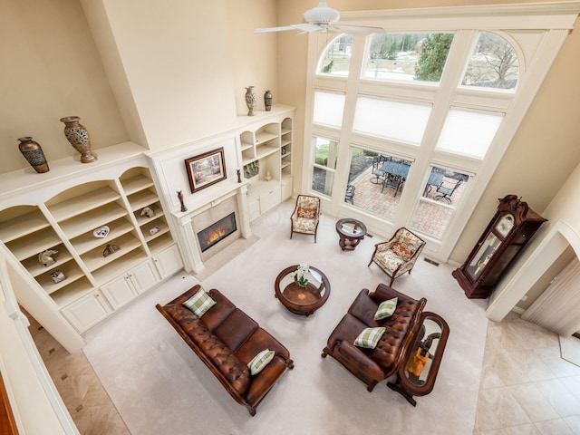 living room with a high ceiling, ceiling fan, light tile patterned floors, and a high end fireplace