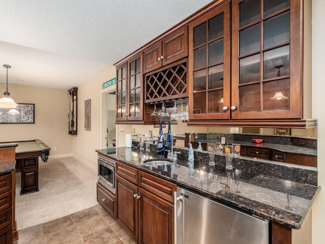 bar featuring sink, dark stone countertops, stainless steel microwave, decorative light fixtures, and light colored carpet