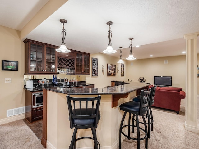 interior space with pendant lighting, stainless steel microwave, light colored carpet, and dark brown cabinets