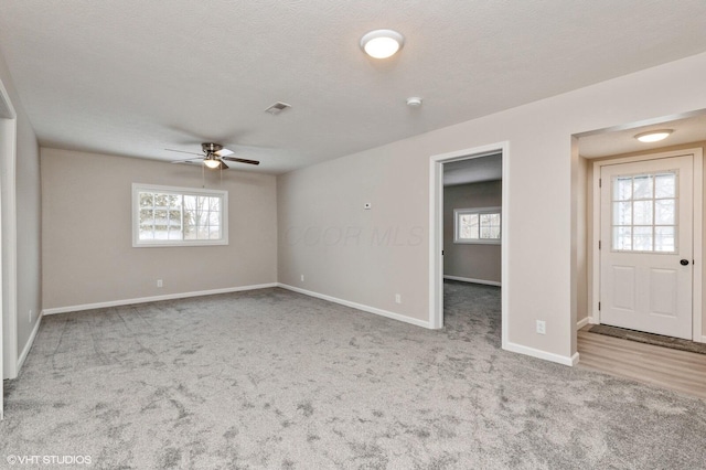 carpeted spare room with a textured ceiling, a wealth of natural light, and ceiling fan