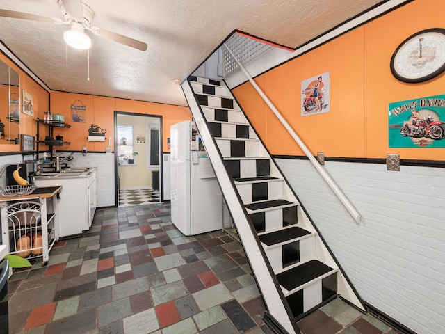 staircase featuring ceiling fan, brick wall, and a textured ceiling