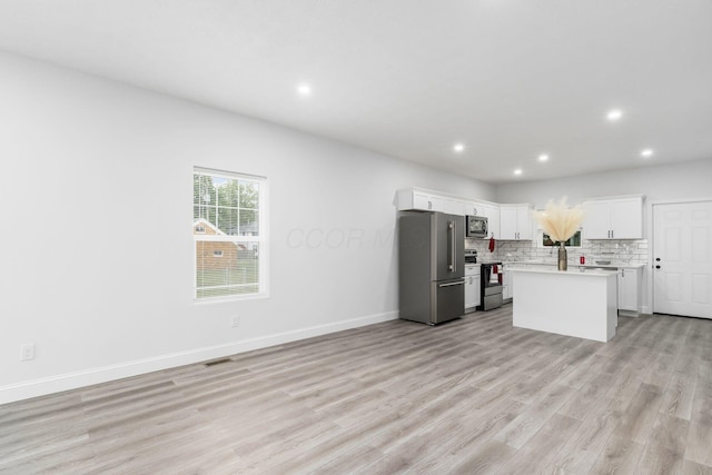 kitchen with a center island, backsplash, light hardwood / wood-style floors, white cabinetry, and stainless steel appliances