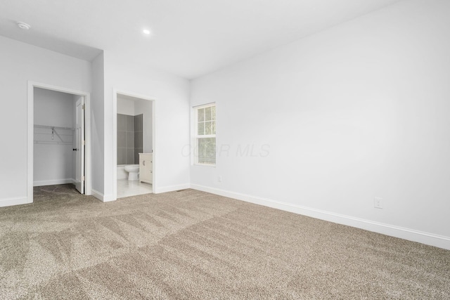 unfurnished bedroom with ensuite bath, a walk in closet, a closet, and light colored carpet