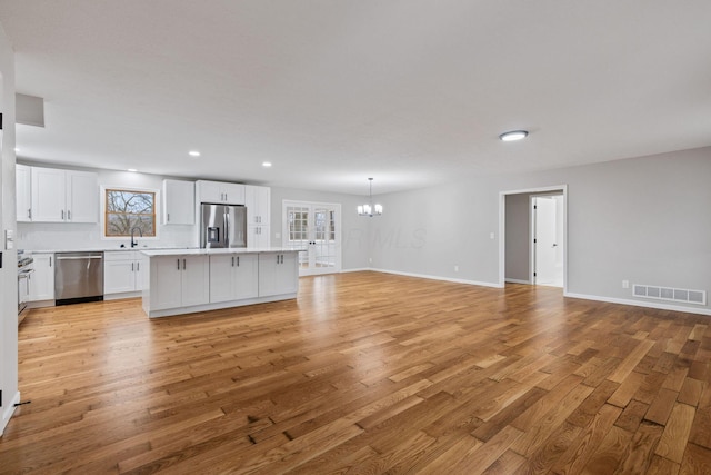 unfurnished living room with an inviting chandelier, sink, and light hardwood / wood-style flooring