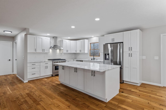 kitchen featuring wall chimney exhaust hood, sink, a kitchen island, stainless steel appliances, and white cabinets