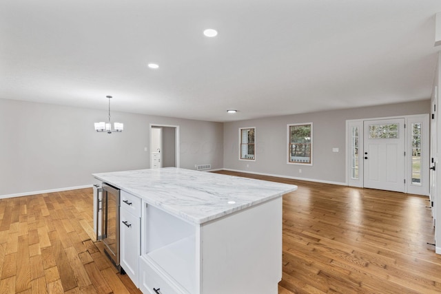 kitchen with wine cooler, light wood-type flooring, a kitchen island, pendant lighting, and white cabinets