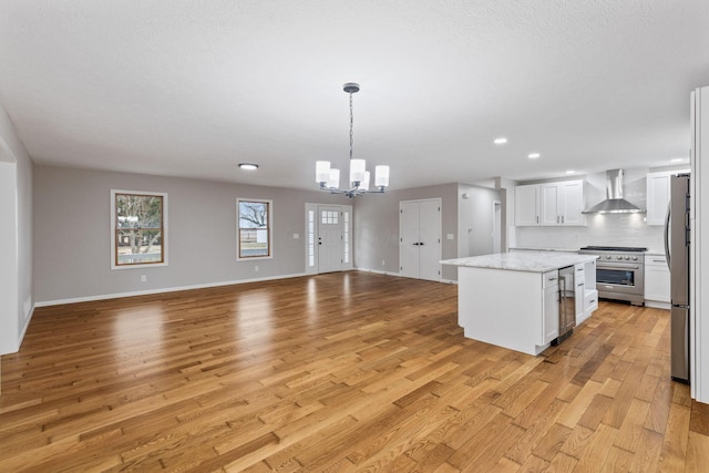 kitchen with pendant lighting, stainless steel appliances, a center island, white cabinets, and wall chimney exhaust hood