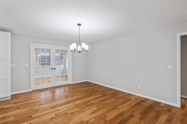 unfurnished dining area featuring a textured ceiling, light hardwood / wood-style flooring, french doors, and a chandelier