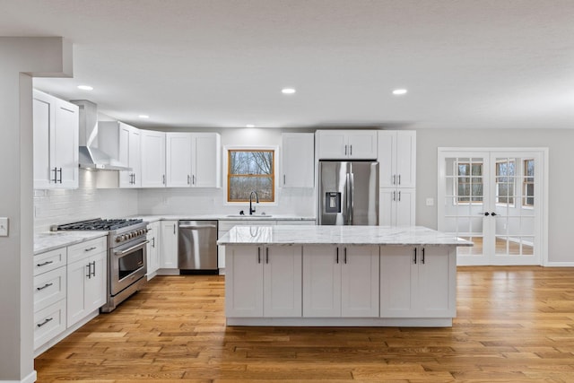 kitchen with stainless steel appliances, white cabinetry, sink, and wall chimney range hood