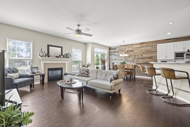 living room with a tile fireplace, wood walls, dark hardwood / wood-style flooring, and ceiling fan with notable chandelier