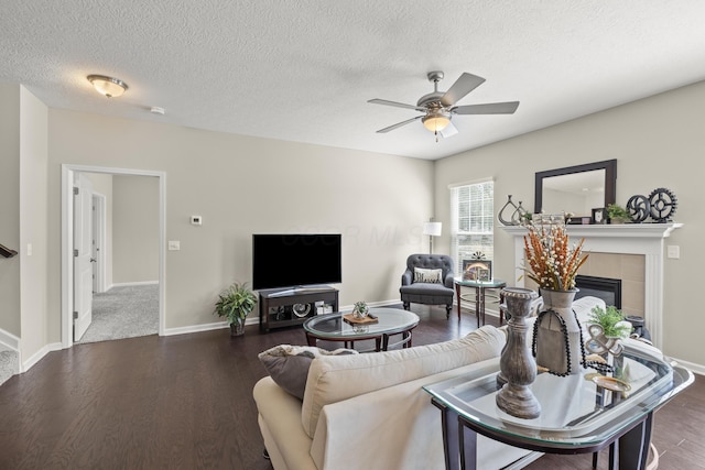 living room featuring a textured ceiling, ceiling fan, dark wood-type flooring, and a tiled fireplace