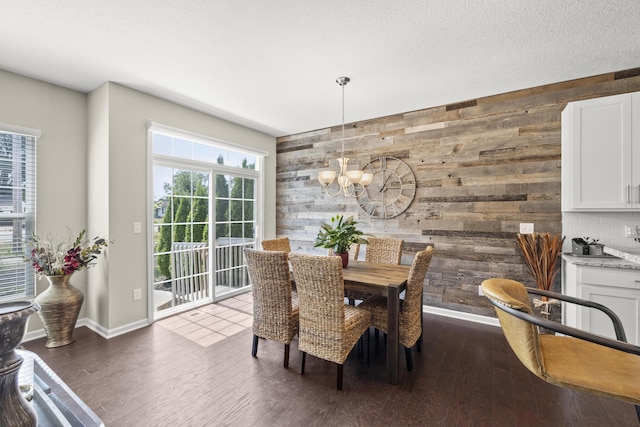 dining space featuring wooden walls, dark wood-type flooring, a textured ceiling, and a notable chandelier