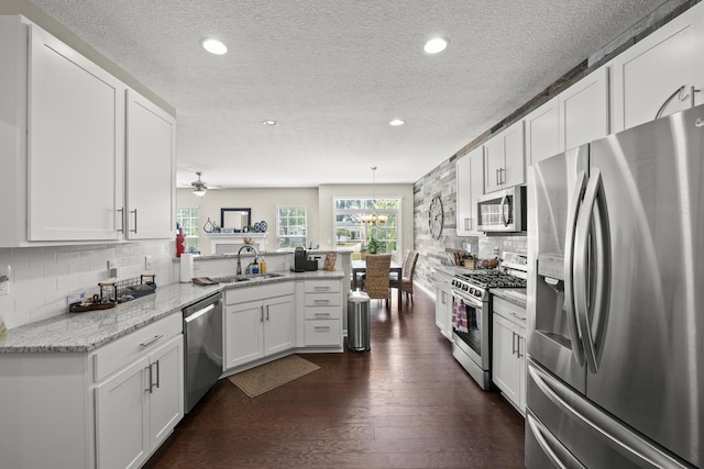 kitchen with kitchen peninsula, light stone counters, stainless steel appliances, sink, and white cabinetry