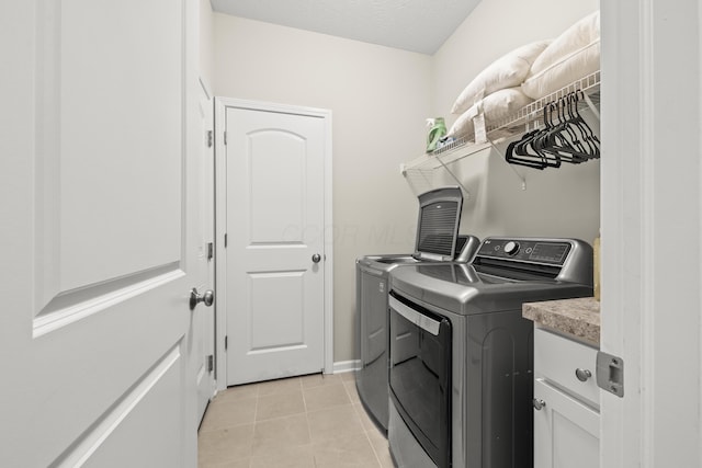 laundry area featuring cabinets, light tile patterned floors, washing machine and dryer, and a textured ceiling