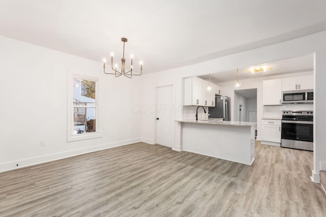 kitchen with white cabinetry, kitchen peninsula, appliances with stainless steel finishes, decorative backsplash, and a chandelier