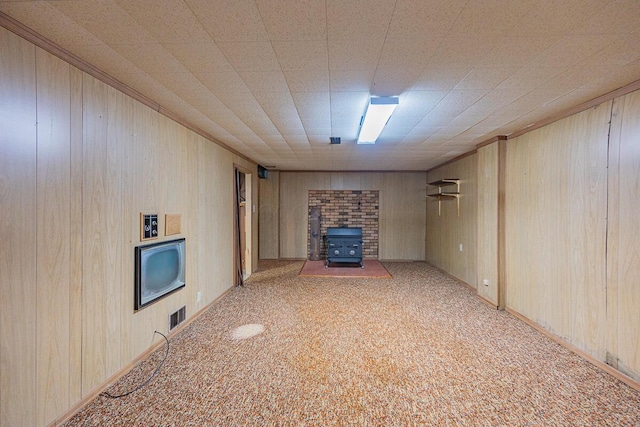 unfurnished living room featuring wood walls, light colored carpet, and a wood stove