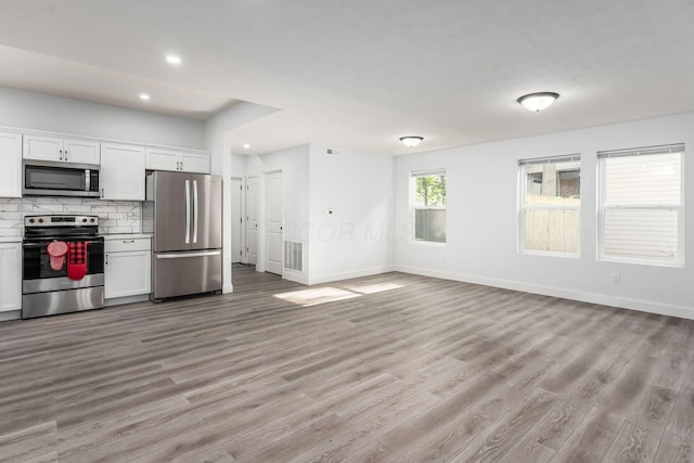 kitchen featuring white cabinetry, decorative backsplash, light wood-type flooring, and appliances with stainless steel finishes