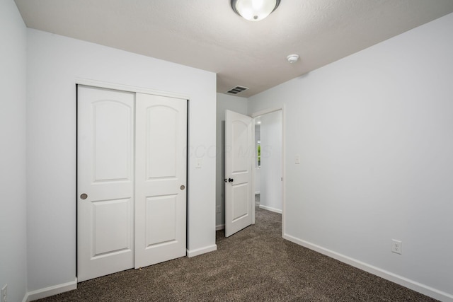 unfurnished bedroom with dark carpet and a closet