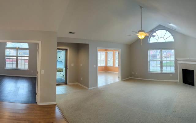 unfurnished living room featuring ceiling fan, light colored carpet, high vaulted ceiling, and a tile fireplace