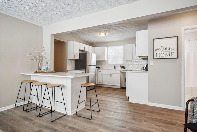 kitchen with white cabinetry, light wood-type flooring, a breakfast bar area, and kitchen peninsula