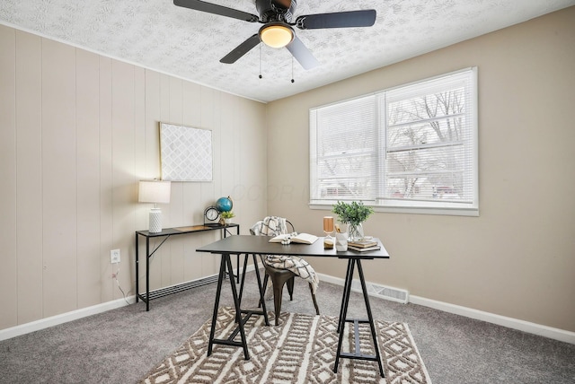 carpeted office featuring a textured ceiling, ceiling fan, and wood walls