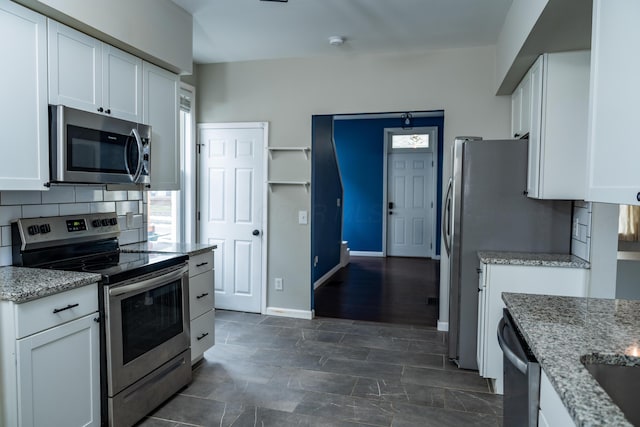 kitchen with light stone counters, backsplash, white cabinetry, and appliances with stainless steel finishes