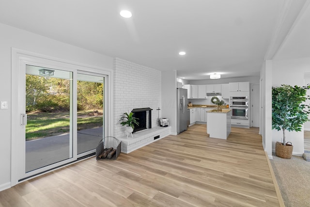 kitchen with a center island, a brick fireplace, light wood-type flooring, stainless steel appliances, and white cabinets