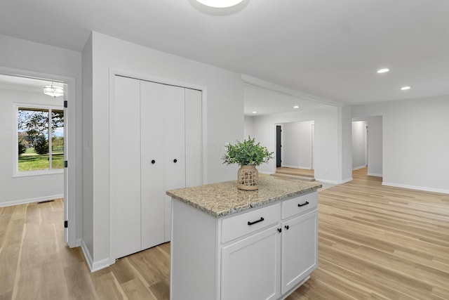 kitchen with white cabinetry, light stone counters, light hardwood / wood-style flooring, and a kitchen island