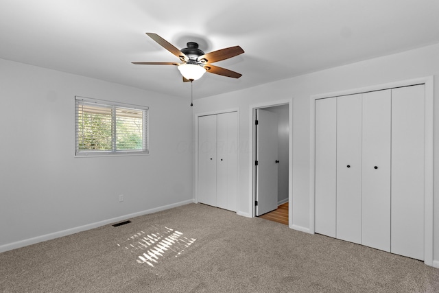 unfurnished bedroom with multiple closets, light colored carpet, and ceiling fan