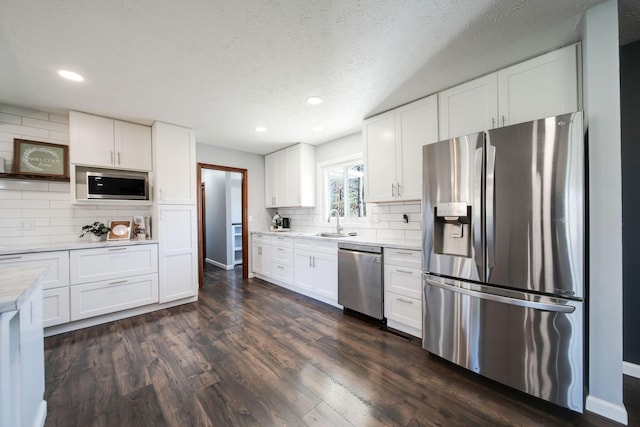 kitchen featuring sink, dark wood-type flooring, backsplash, stainless steel appliances, and white cabinets