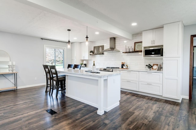 kitchen featuring pendant lighting, white cabinets, a center island, stainless steel appliances, and wall chimney exhaust hood