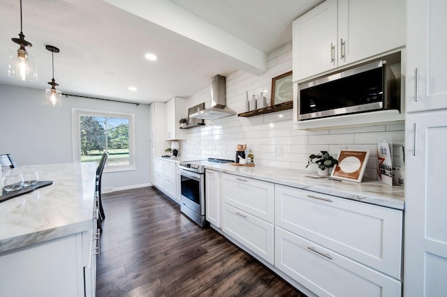 kitchen with appliances with stainless steel finishes, pendant lighting, white cabinets, and wall chimney exhaust hood