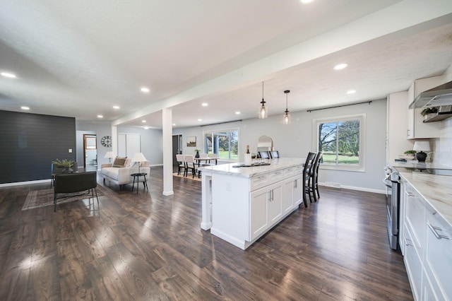 kitchen with light stone counters, decorative light fixtures, electric stove, a kitchen island with sink, and white cabinets