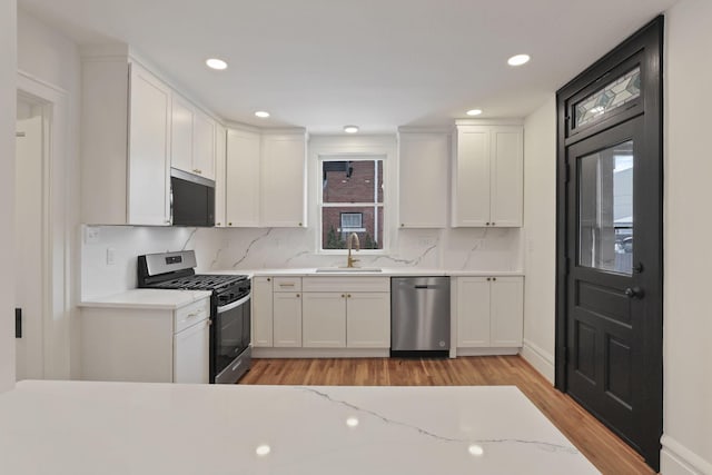 kitchen featuring light stone countertops, light wood-type flooring, stainless steel appliances, sink, and white cabinetry