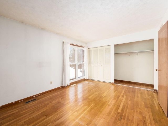 unfurnished bedroom with a textured ceiling, light wood-type flooring, and multiple closets