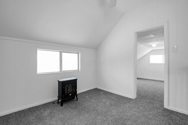 additional living space with a wood stove, lofted ceiling, a textured ceiling, and dark colored carpet