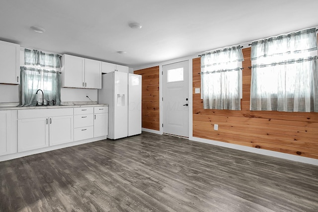 kitchen with white cabinetry, sink, white fridge with ice dispenser, plenty of natural light, and wooden walls