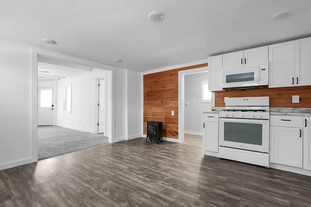 kitchen with white appliances, white cabinetry, a wood stove, and wooden walls