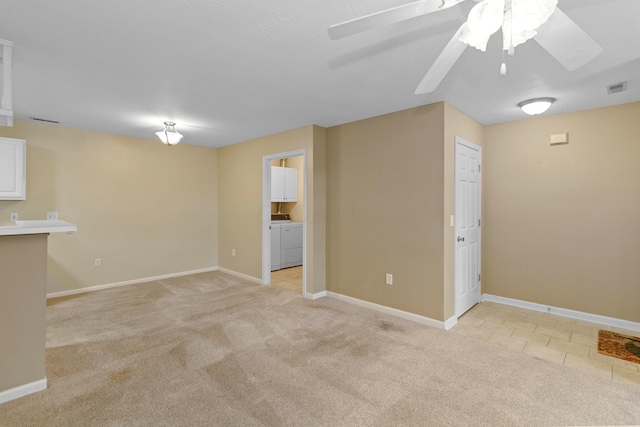 unfurnished room featuring light carpet, ceiling fan, and washer and dryer