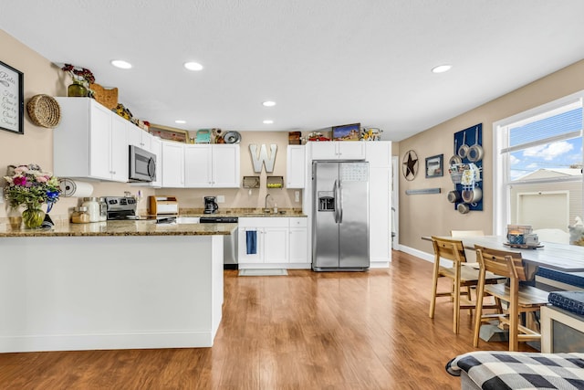 kitchen with kitchen peninsula, appliances with stainless steel finishes, sink, dark stone countertops, and white cabinets