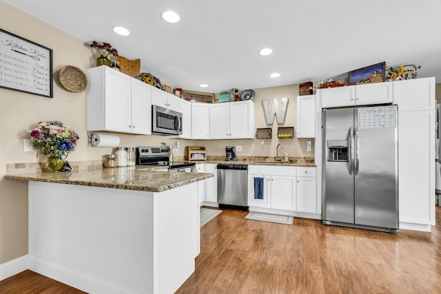 kitchen featuring kitchen peninsula, appliances with stainless steel finishes, white cabinets, and light hardwood / wood-style flooring