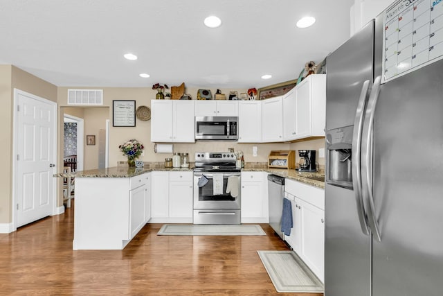 kitchen with kitchen peninsula, appliances with stainless steel finishes, dark stone countertops, white cabinets, and hardwood / wood-style floors