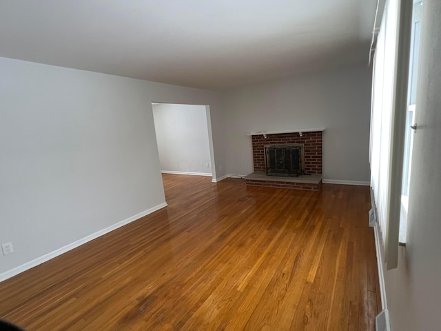 unfurnished living room with hardwood / wood-style floors and a brick fireplace