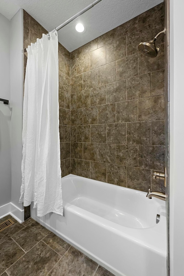 bathroom with a textured ceiling and shower / tub combo with curtain