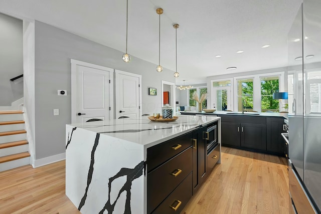 kitchen with pendant lighting, a large island, light hardwood / wood-style floors, and light stone countertops