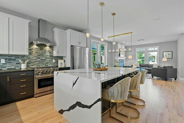 kitchen with white cabinets, wall chimney exhaust hood, pendant lighting, and appliances with stainless steel finishes