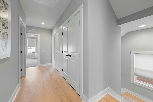 hallway with light wood-type flooring and vaulted ceiling