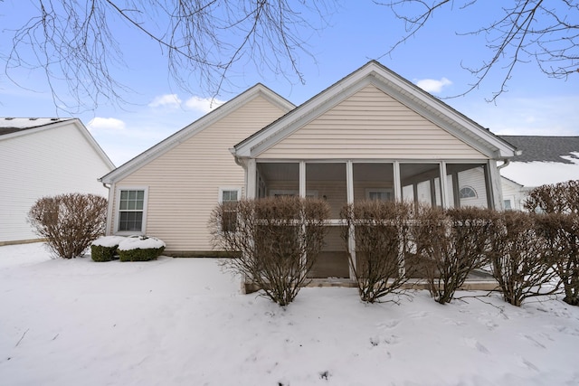 snow covered back of property featuring a sunroom