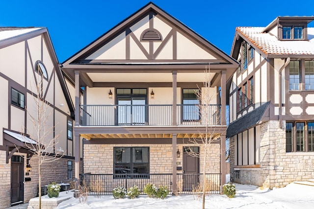 tudor-style house featuring covered porch and a balcony