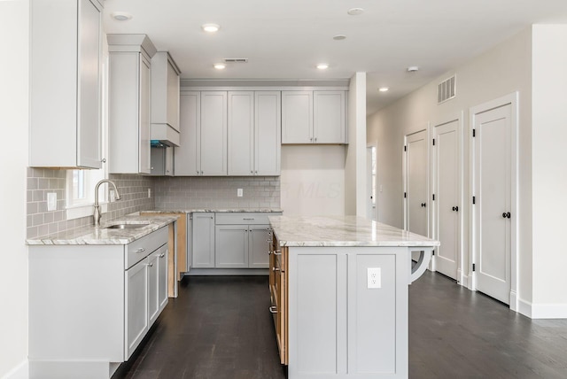 kitchen featuring sink, dark hardwood / wood-style floors, tasteful backsplash, a kitchen island, and light stone counters